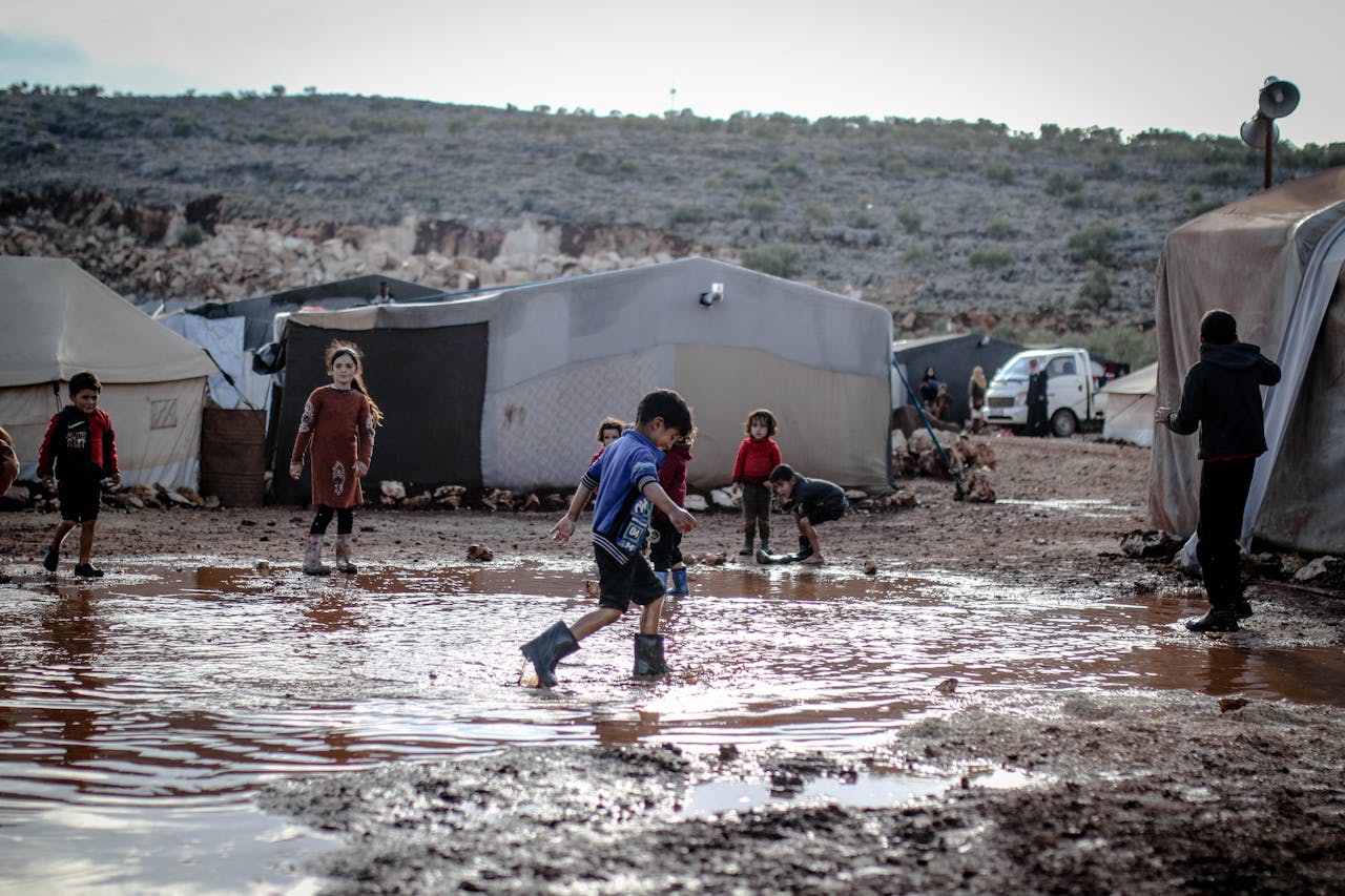 services-03 Children play in a muddy area within a refugee camp in Idlib, Syria, showcasing resilience amid challenging conditions.